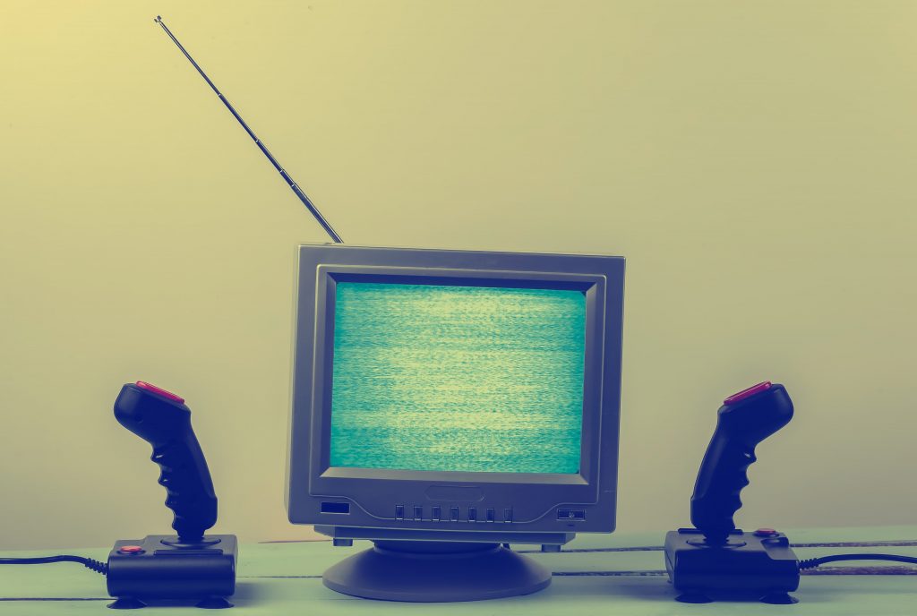 Televisão pequena de tubo com a tela fora do ar, com dois joysticks de Atari de cada lado do aparelho.