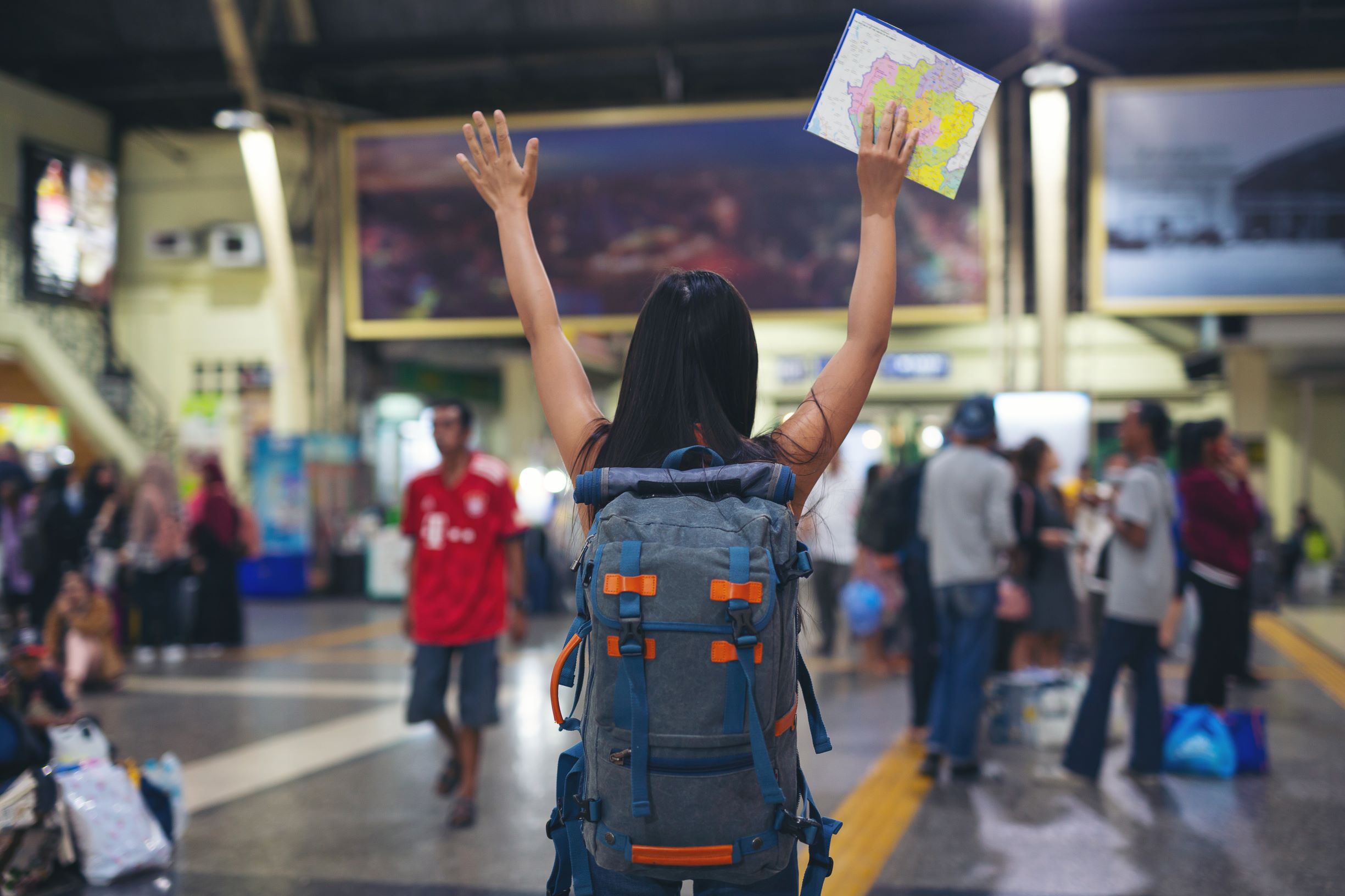 Foto de uma mulher de costas, com as mãos para o alto, segurando um mapa em uma das mãos e com uma mochila nas costas. A foto foi tirada em um aeroporto, demonstrando as múltiplas possibilidades de uma cidade digital.