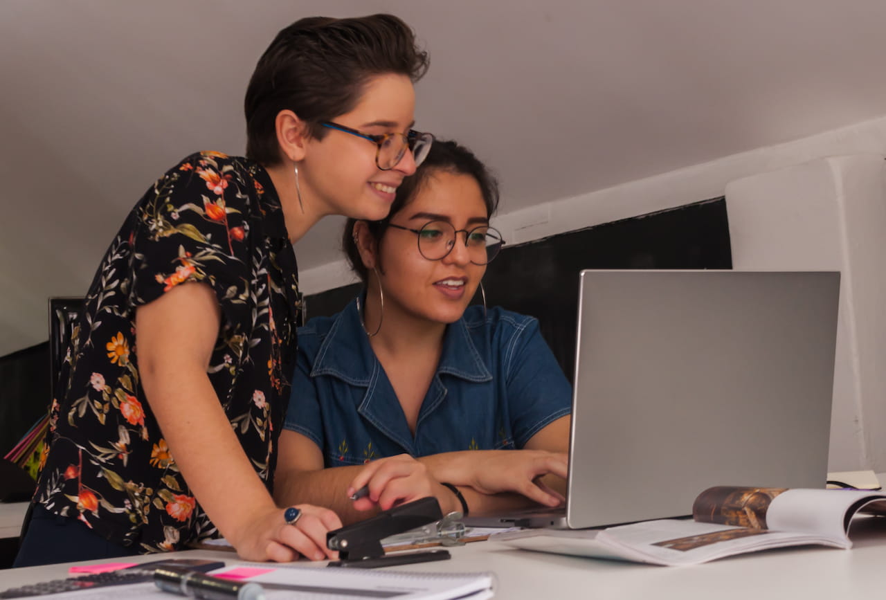 Duas mulheres, uma sentada e outra em pé, olhando para um laptop