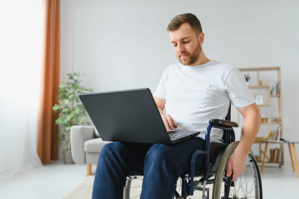 Homem branco em cadeira de rodas mexendo em um notebook em seu colo