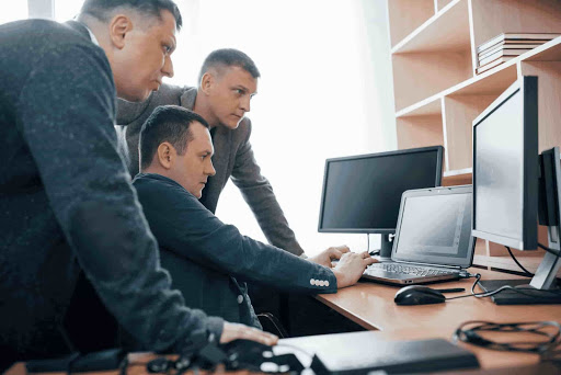3 homens de paletó em uma sala de reunião, observando a tela de um computador