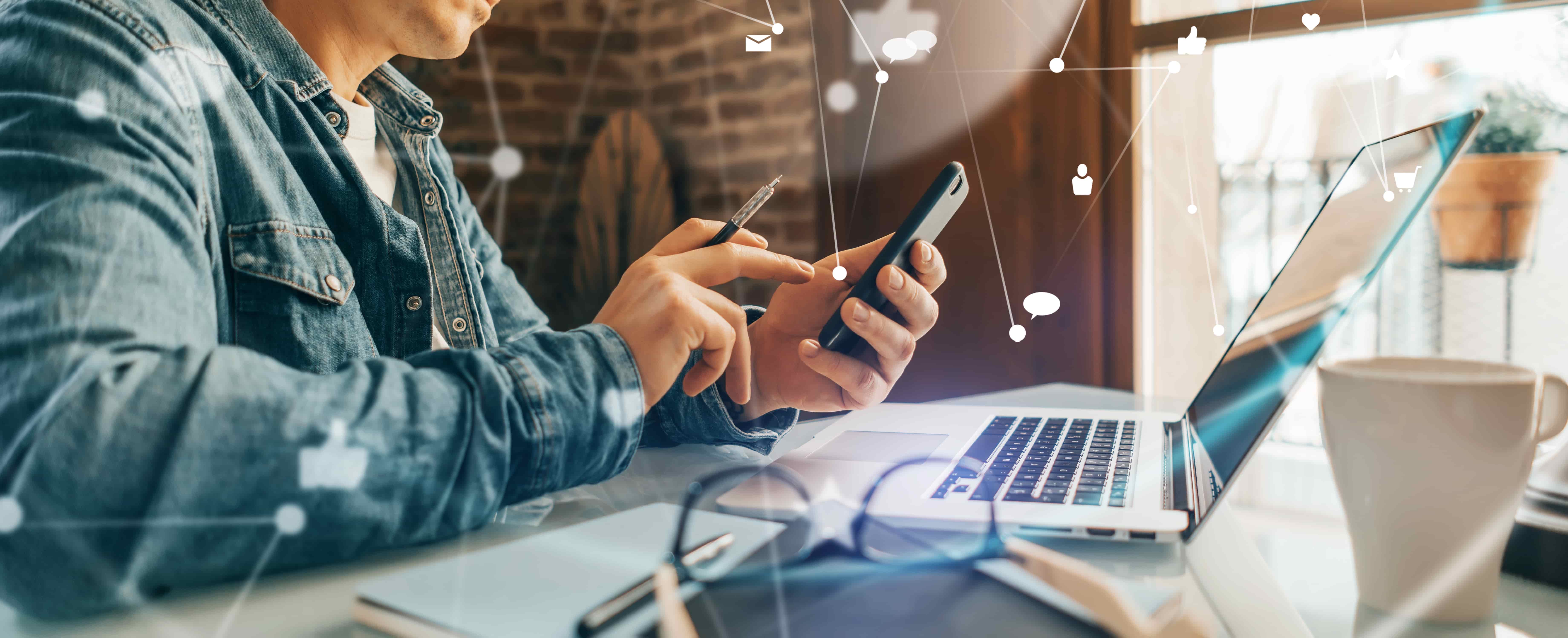 Homem usando smartphone e notebook em segurança. Sentando em mesa de escritório