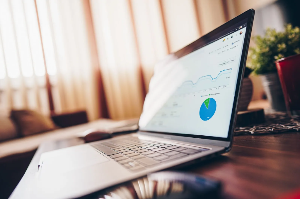 Um notebook aberto apoiado em uma mesa de madeira, com gráficos projetados em sua tela.