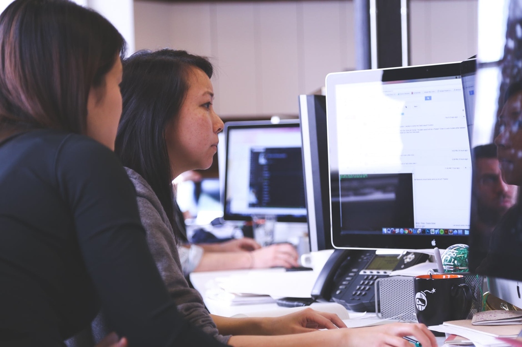 Duas mulheres sentadas em frente de um computador trabalhando. 