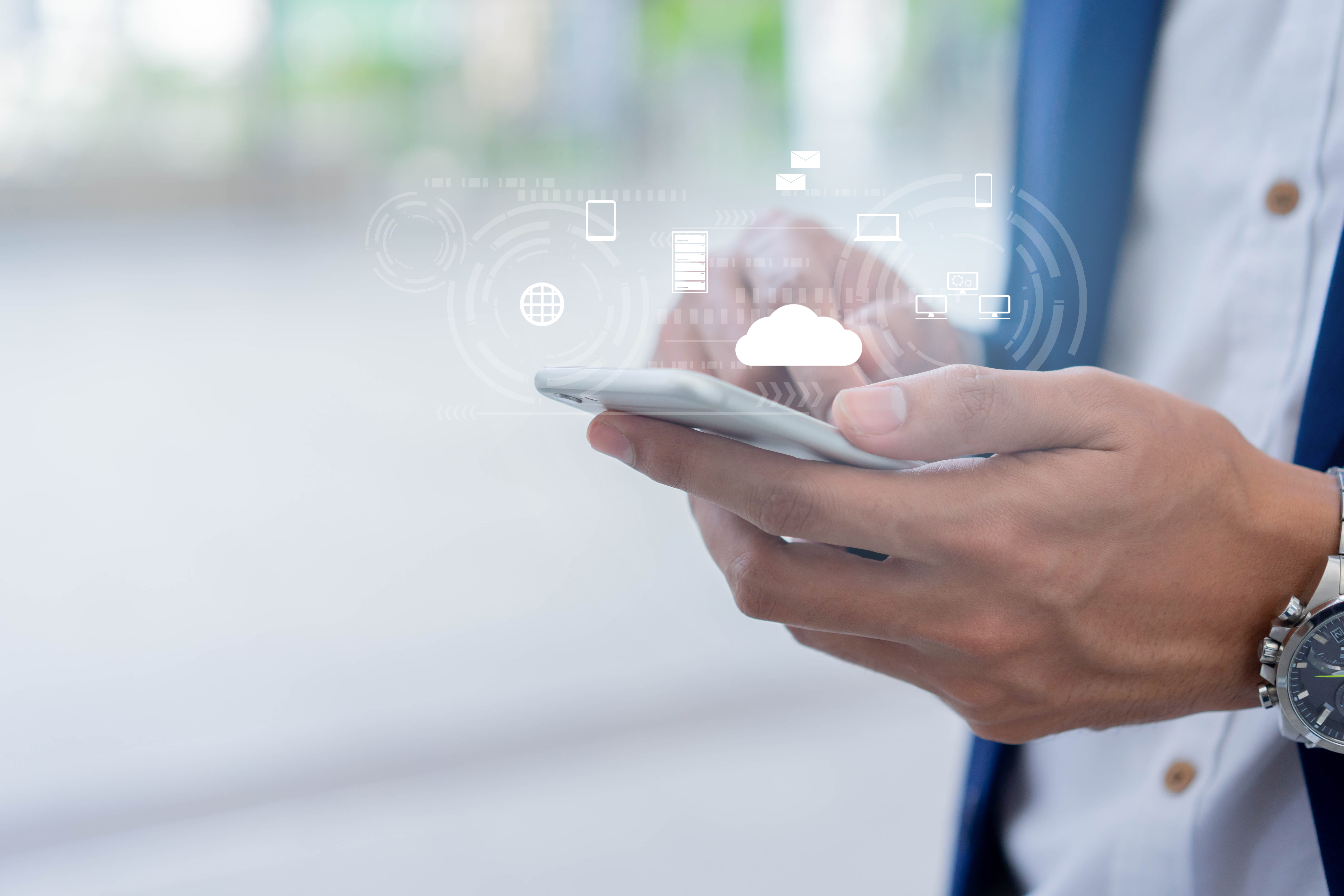  Homem de terno manuseando smartphone do qual saem alguns símbolos que remetem ao universo digital. 