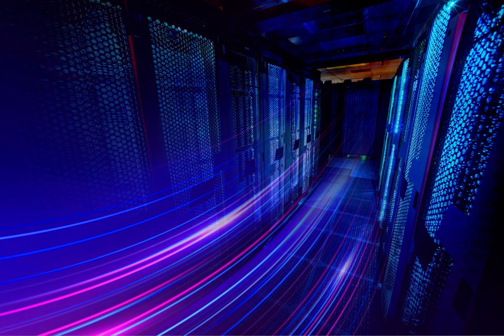 : Imagem de uma fotografia em que há uma sala de data center em cores como azul, roxo e rosa.
