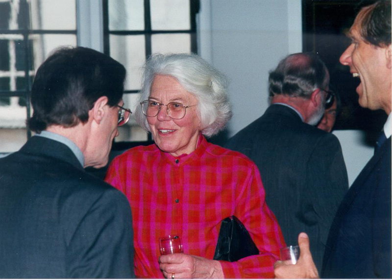 Imagem de uma fotografia de uma mulher de idade de cabelos curtos e brancos, ela usa óculos e uma roupa vermelha.