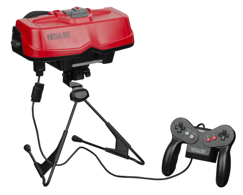 Imagem de uma fotografia com fundo branco em que há um óculos grande apoiado em um tripé e conectado a um controle de videogame. No óculos e no controle está escrito “virtual boy”.
