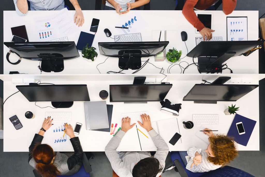 Um escritório visto de cima, com pessoas sentadas de frente para seus computadores enquanto trabalham com um financiamento de projeto. 