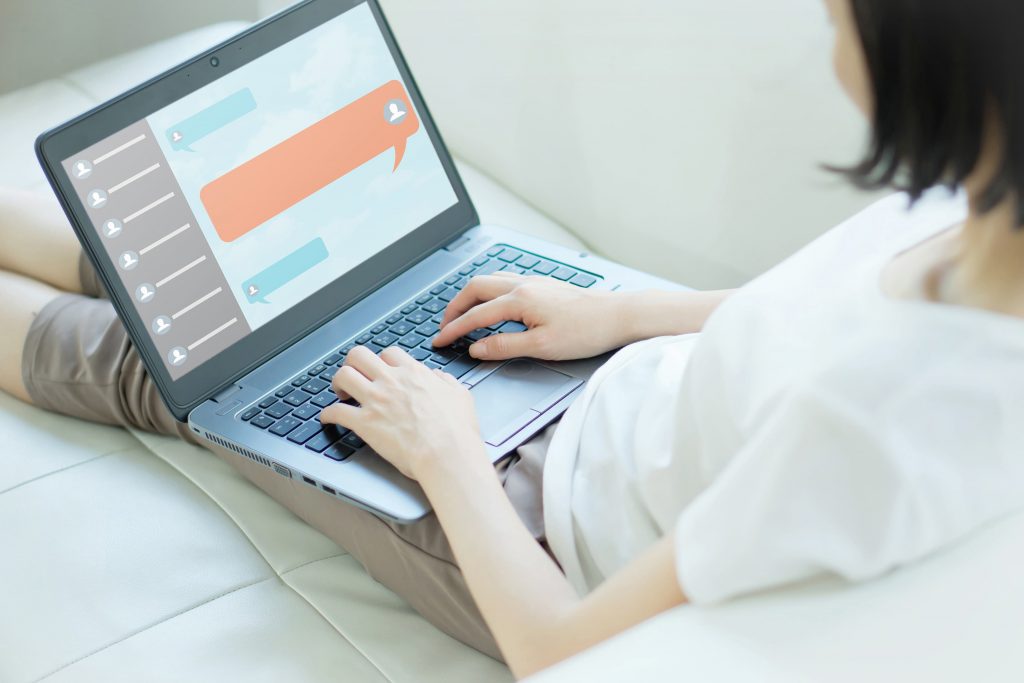 mulher com um notebook ao colo, e na tela uma janela de diálogo com um chatbot