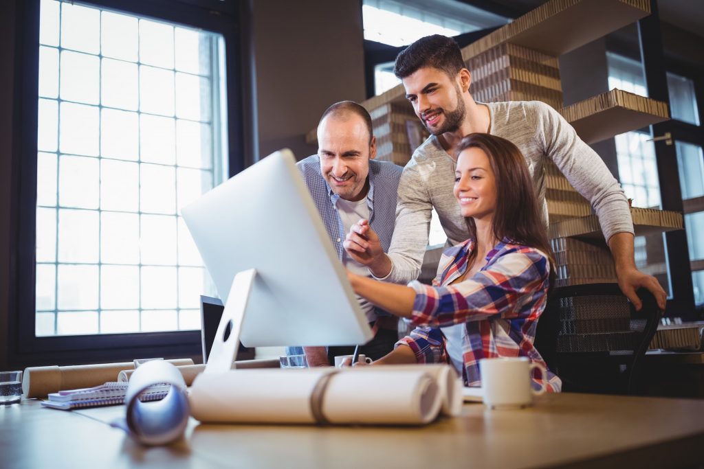 Uma mulher e dois homens brancos de frente para um computador em um escritório.