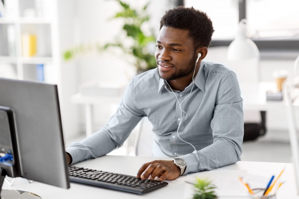 Homem negro sentado de frente para um computador, com fones de ouvido, enquanto faz um curso de cloud. 