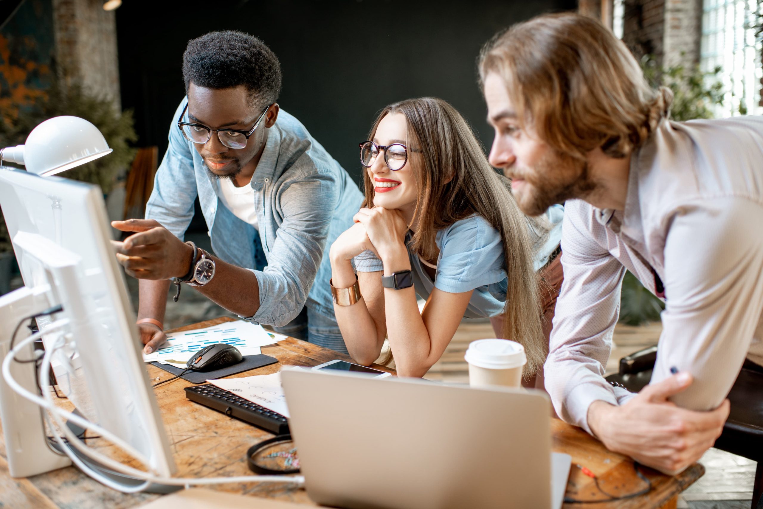 plataforma omnichannel capa Um homem negro, um homem branco e uma mulher branca de óculos em frente a um computador em um escritório, vendo sobre plataforma omnichannel