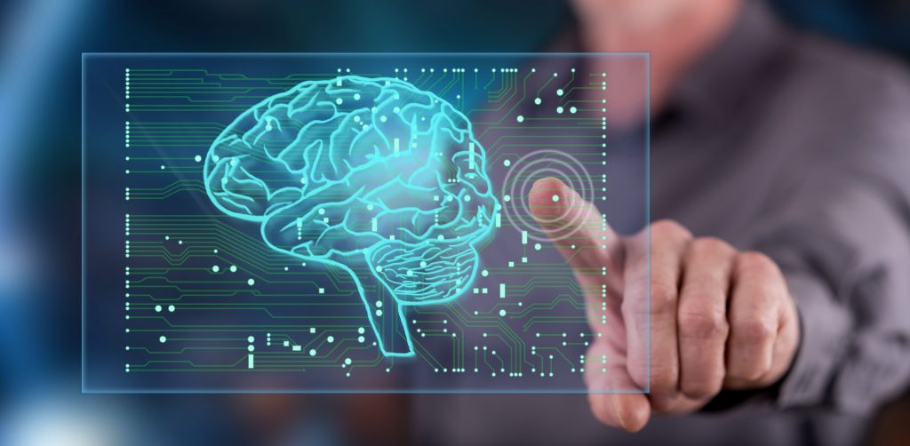 dedo indicador de uma pessoa branca toca uma tela holográfica que projeta o contorno de um cérebro.
