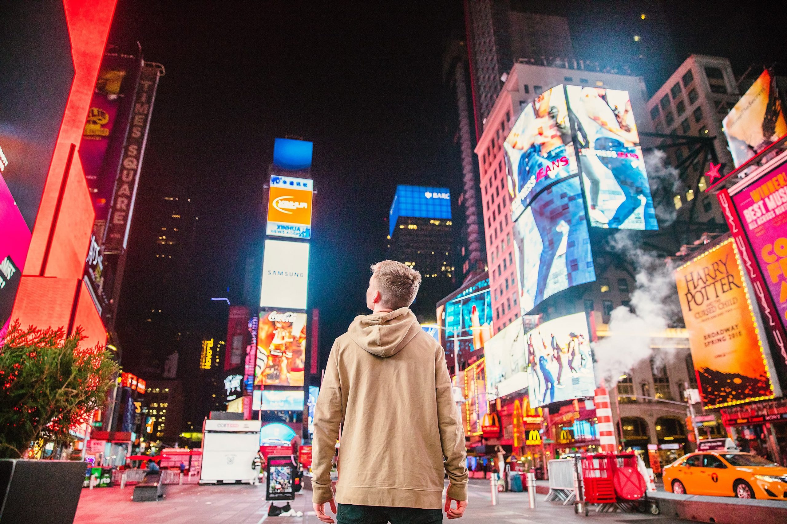 Rapaz branco de costas encara uma série de telas de sinalização na Times Square, de Nova York.