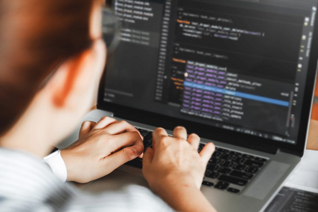 Mãos de uma pessoa branca digitando em um notebook e criando códigos para back end.