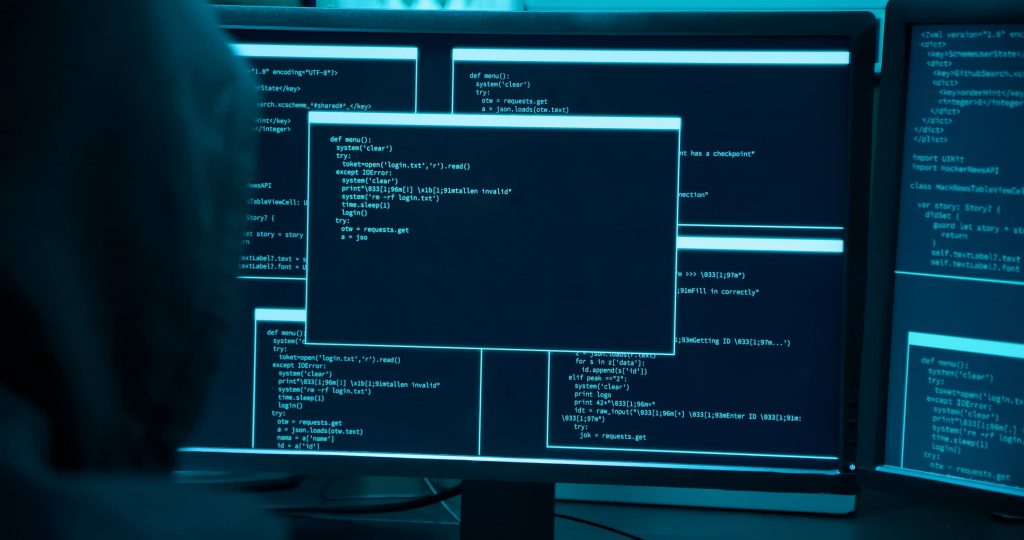 Telas de computador com diferentes janelas de códigos sob uma luz azulada.