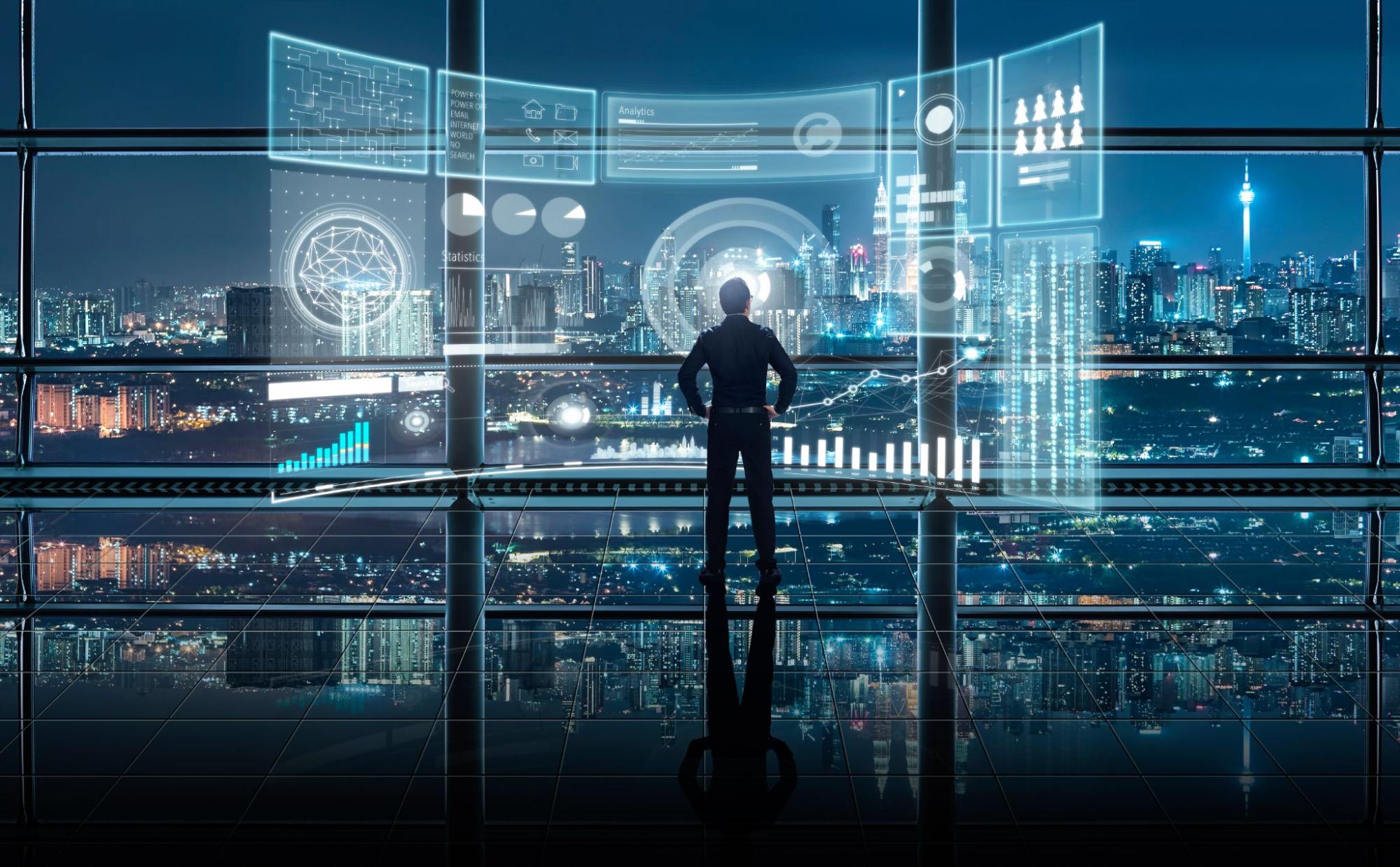 Metadados capa pessoa de costas analisa a projeção digital de uma tela com gráficos e demais dados. Ao fundo, janelas de vidro mostram a vista de uma cidade à noite.