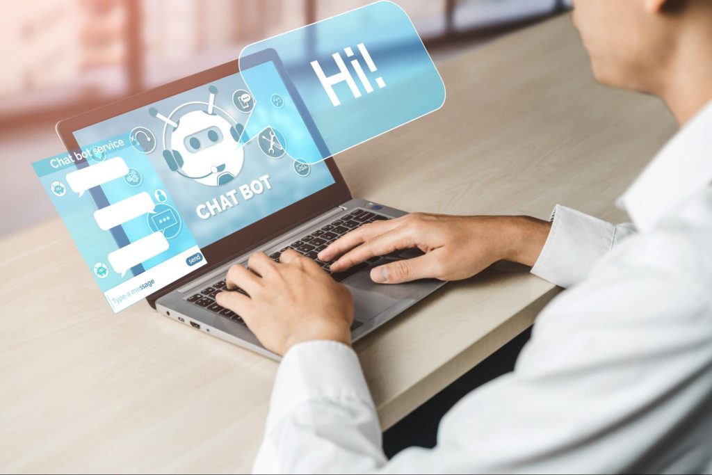 homem branco vestindo camisa social branca digita em notebook com símbolos relacionados a chatbots