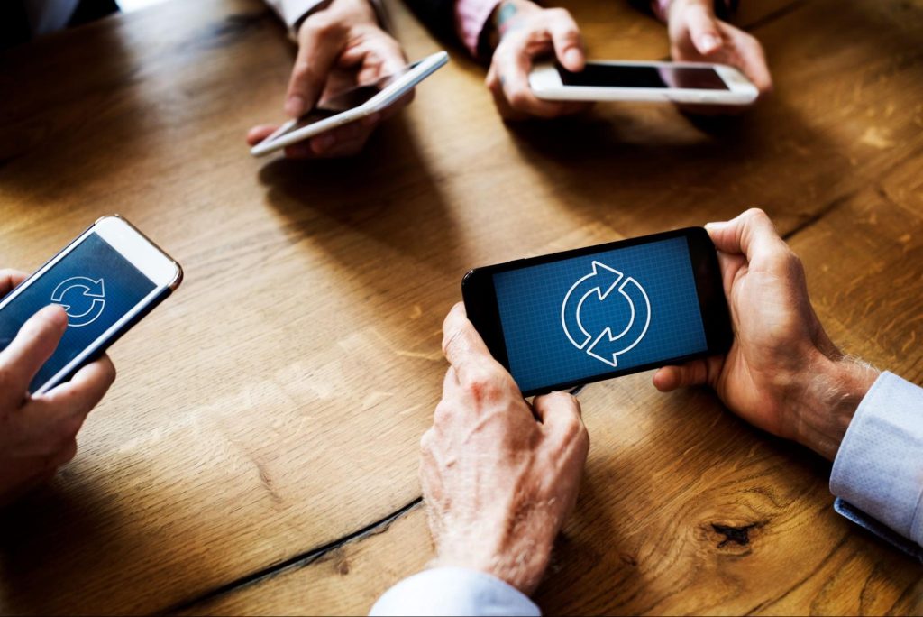 mãos humanas segurando celular com símbolo qiue representa o ciclo de reuso de produtos e matéria-prima