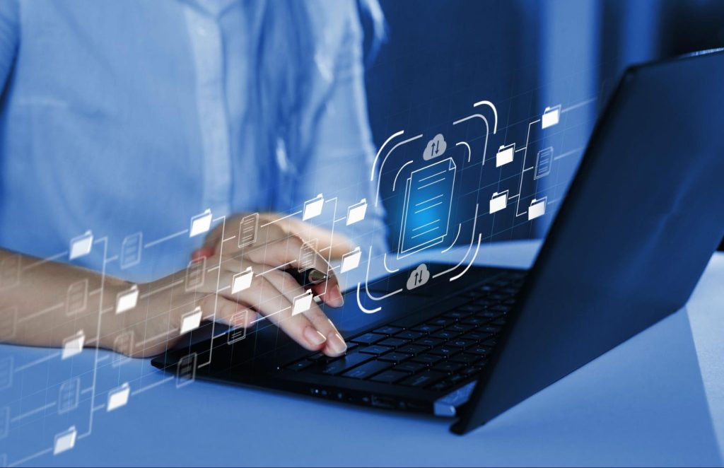 : profissional de qualidade do software veste camisa azul e está digitando em notebook escuro. Desenhos de arquivos sendo transportados em linhas claras sobrepõem a imagem